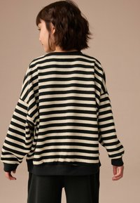 Sweatshirt rayé noir et blanc cassé avec un col rond, des épaules tombantes et des poignets côtelés ; texture douce et coupe ample.