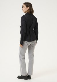 Camicia nera con bottoni, dal design strutturato, maniche lunghe e piega sul retro. Indossata con jeans dritti grigio chiaro e scarpe nere chunky.