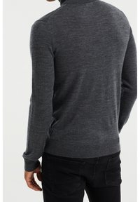 Dark gray knit sweater with a high neckline, fitted sleeves, and ribbed hem. Worn over black pants, showing a textured finish.