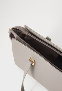 Graue, strukturierte Handtasche mit einem Reißverschlussverschluss, goldenen Hardware-Elementen und einem verstellbaren Tragegurt. Das Innenleben umfasst mehrere Fächer.