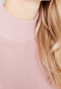 Top rosa chiaro a coste con collo alto, caratterizzato da una fine trama e una finitura liscia. La ripresa ravvicinata mostra i dettagli del tessuto senza elementi aggiuntivi.