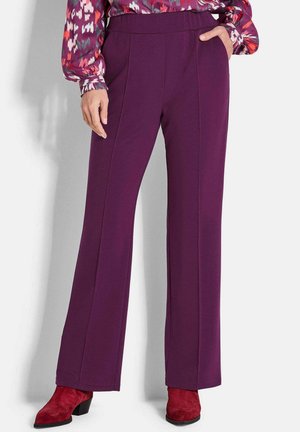 Vrouw in hoge taille, straight-leg paarse broek, gecombineerd met een patronen lange mouwen top en rode suède enkellaarsjes.