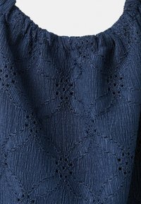 Tessuto blu navy con motivo a diamante strutturato e piccoli dettagli a occhiello, raccolto lungo il bordo superiore con una caduta morbida.