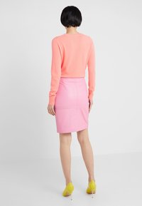 Gonna di pelle rosa brillante, design aderente, abbinata a un morbido maglione corallo. L'outfit presenta tacchi alti gialli e una superficie liscia.
