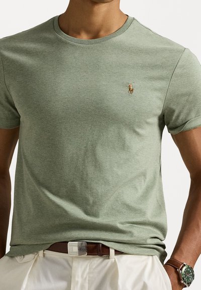 Πράσινο βαμβακερό μπλουζάκι με στρογγυλή λαιμόκοψη. Διαθέτει ένα μικρό κεντητό λογότυπο αλόγου στο στήθος. Συνδυάζεται με καφέ ζώνη και λευκά παντελόνια.