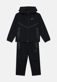 Črn Nike trenirki, sestavljen iz zadrge z kapuco z podloženo zasnovo in hlač z vključnimi žepi. Mehka tkanina z mat končnim videzom.