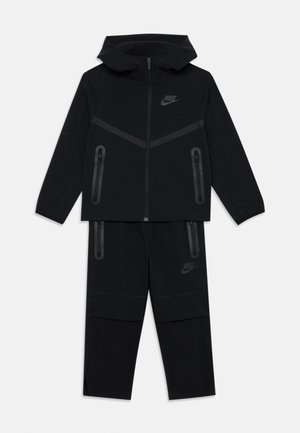 Tuta Nike nera composto da una felpa con zip e un design a righe e pantaloni con tasche con zip. Tessuto morbido con finitura opaca.