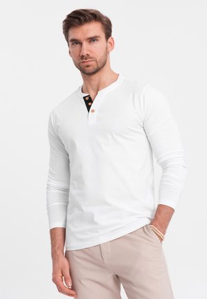 Maglietta henley bianca a maniche lunghe con colletto nero e tre bottoni in legno, realizzata in morbido cotone.