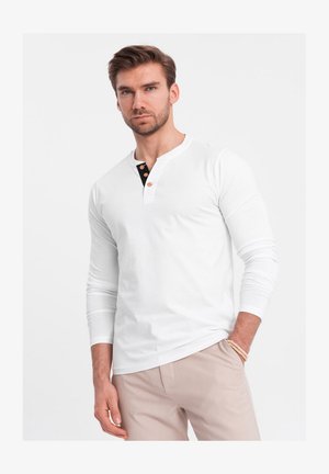 Chemise henley blanche à manches longues avec un col noir, ornée de trois boutons en bois, confectionnée en doux tissu en coton.