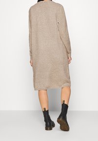 Béžové pletené šaty s dlouhými rukávy, střední délky, s uvolněným střihem. V kombinaci s černými kotníkovými botami s texturovanou podrážkou a poutky.