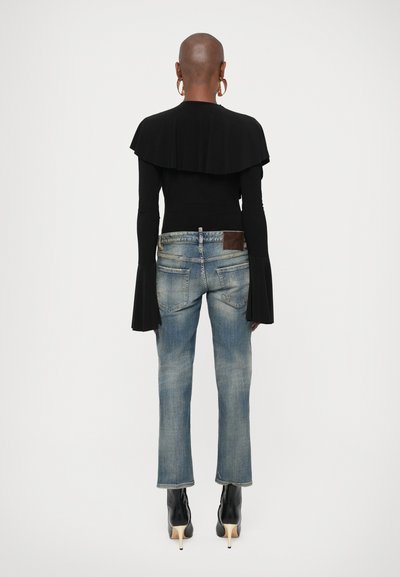 Μαύρο τοπ με μακριά μανίκια και βολάν στον λαιμό, συνδυασμένο με μπλε τζιν καμπάνα και μαύρα μποτάκια με τακούνι. Η πίσω όψη δείχνει λεπτομέρειες του τοπ και των τζιν.