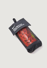 Espinilleras Nike Mercurial Flylite Superlock, en rojo y negro, en una funda transparente, con orificios de ventilación y una parte superior negra con marca.
