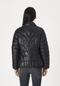 Giacca a vento nera con collo alto, caratterizzata da cuciture geometriche trapuntate, cuciture orizzontali e una texture lucida e liscia.