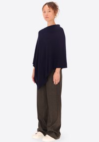 Poncho navy a forma triangolare, realizzato in tessuto morbido. Abbinato a pantaloni a quadri a gamba larga e scarpe da ginnastica bianche. Design minimalista.