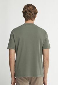 Olivgrön kortärmad t-shirt med rund hals, slätt bomullsmaterial och rak skärning. Inga synliga mönster eller detaljer.