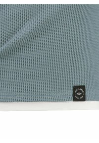 Tessuto azzurro chiaro con texture a nido d'ape. Il bordo presenta una fodera bianca e un'etichetta nera con la scritta "Key Largo dal 1994."