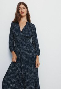 Langes navyblaues Kleid mit langen Puffärmel, einem tiefen V-Ausschnitt und elastischem Bund. Verfügt über ein dezentes geometrisches Muster im gesamten Kleid.