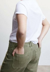 Olijfgroene jeans met achterzakken en riemlussen, gecombineerd met een witte t-shirt met korte mouwen, gezien van achteren. Glad stofoppervlak.