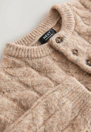 Pull en tricot beige en laine texturée avec col côtelé et motif de câble détaillé, doté de fermetures à boutons marron et d'une étiquette de marque.