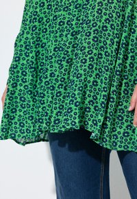 Top a stampa floreale verde con fiori blu navy, tessuto leggero, design fluido e dettagli arricciati. Abbinato a denim blu scuro.