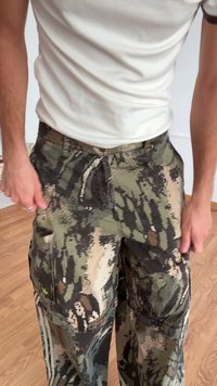 Pantalones cargo de camuflaje que presentan una mezcla de tonos verdes y marrones, múltiples bolsillos y un corte holgado. La tela tiene un patrón texturizado.