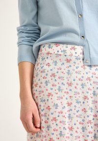 Lyseblå strikket cardigan med rund hals, parret med en nederdel med blomsterprint med små lyserøde og blå blomster på en cremet baggrund.