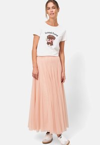 Weißes T-Shirt mit "Cocktail Friday" Grafik, kombiniert mit einem luftigen, hellrosa Tüllrock und weißen Sneakern. Weiche Texturen und plissiertes Design.
