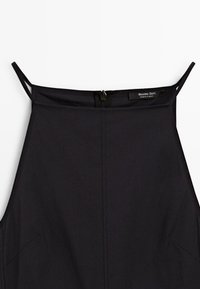 Černý top bez rukávů s tenkými ramínky, vybavený zipem na zadní straně a minimalistickým designem. Látka se zdá být hladká s matným povrchem.