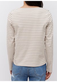 Beżowa bluzka z długim rękawem z kremowymi poziomymi paskami. Posiada okrągły dekolt i miękką, gładką fakturę. Połączona z niebieskimi dżinsami.