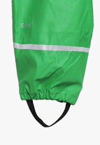 Capa de chuva verde, impermeável, com fundo franzido e tira elástica preta. Apresenta uma faixa refletora prateada para visibilidade.