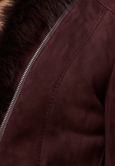 Chaqueta de ante burdeos con cuello de piel sintética, cierre de cremallera y detalles cosidos a lo largo de las costuras, con una textura suave.