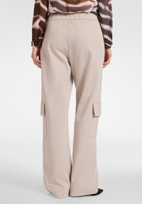 Beige wijde broek heeft een zachte textuur, een elastische tailleband en cargozakken aan beide zijden voor extra functionaliteit.