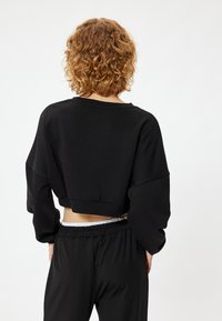 Czarna skórzana bluza z długim rękawem, ściętą talią i luźnym krojem, połączona z czarnymi spodniami z elastycznym pasem.