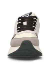 Vue de face d'une sneaker beige et grise avec des lacets noirs et une semelle noire, featuring des symboles triangulaires et "X".