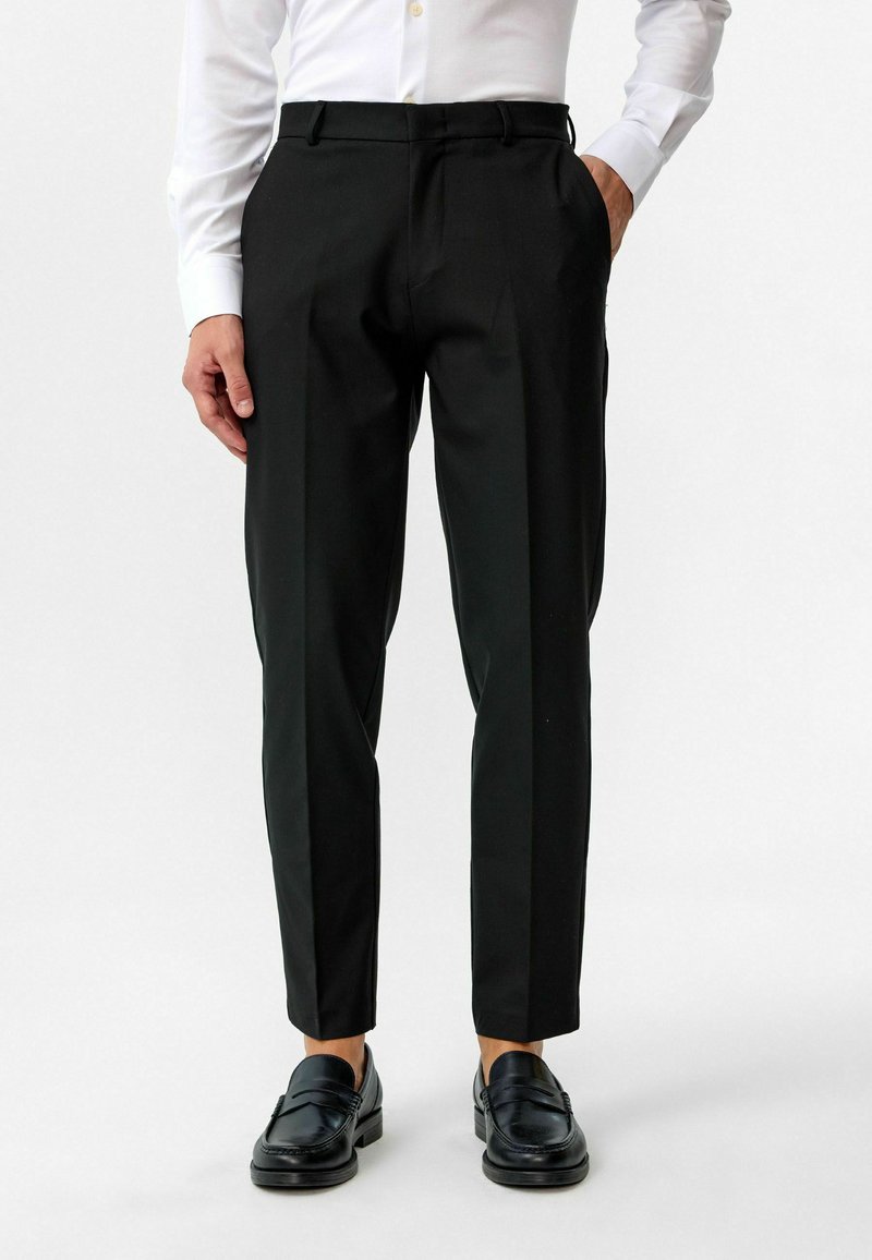 Zwarte op maat gemaakte broek met een slanke pasvorm, voorzien van zijzakken, een vlakke voorkant en een gladde textuur, gecombineerd met zwarte instappers.