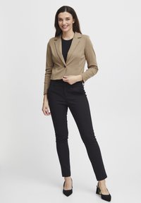 Tan blazer med en figursydd design, enkel knappstängning och långa ärmar, i kombination med svarta slim-fit byxor och svarta högklackade skor.