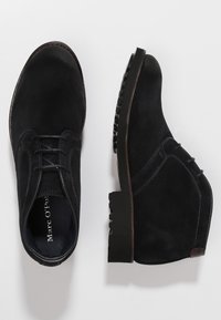 Scarpe nere in suede con una texture liscia, design con lacci, punta rotonda e suola spessa e testurizzata con dettagli di cucitura laterale.
