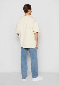 Kremfarget oversized t-skjorte med korte ermer, kombinert med lyseblå, rette jeans, som viser et enkelt design og en avslappet passform.