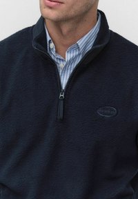 Granatowy polarowy sweter z zamkiem przy kołnierzu, z teksturowanym wykończeniem i małym haftowanym logo na klatce piersiowej.