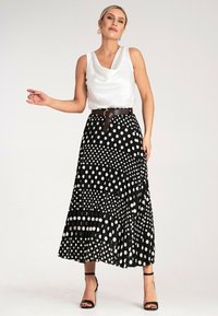 Biała satynowa bluzka z dekoltem w kształcie płaszcza zestawiona z czarną plisowaną spódnicą w różnej wielkości białe kropki, przewiązana brązowym paskiem.