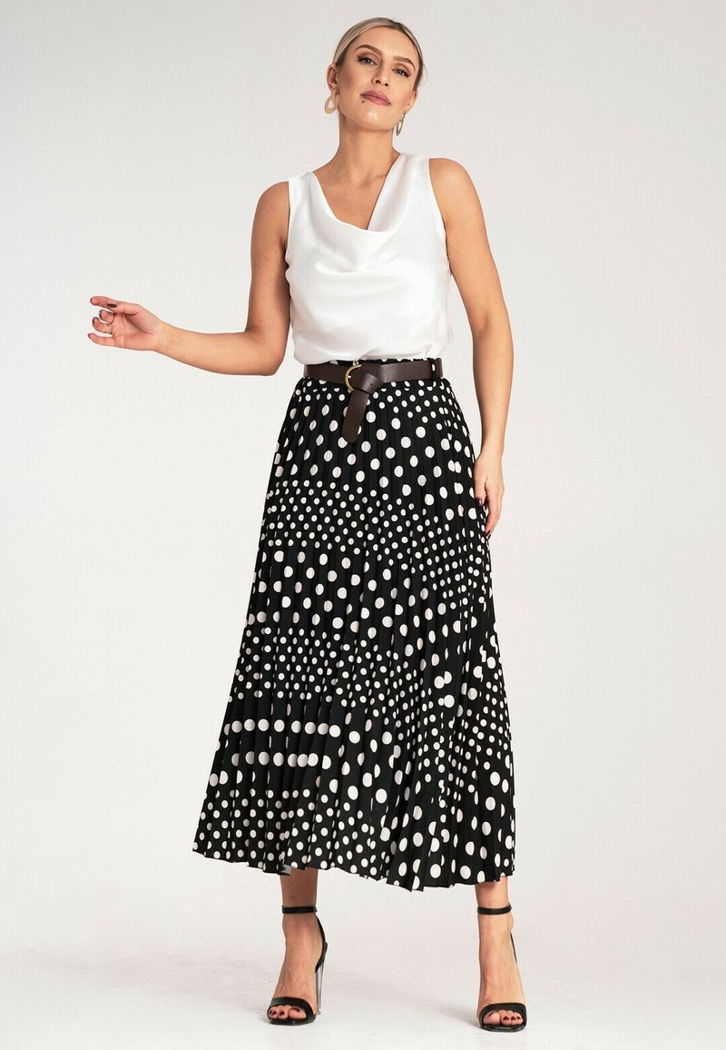 Biała satynowa bluzka z dekoltem w kształcie płaszcza zestawiona z czarną plisowaną spódnicą w różnej wielkości białe kropki, przewiązana brązowym paskiem.