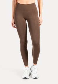 Leggings marroni a vita alta con una texture liscia, caratterizzate da cuciture laterali sottili e una cintura a coste, abbinate a scarpe sportive bianche.