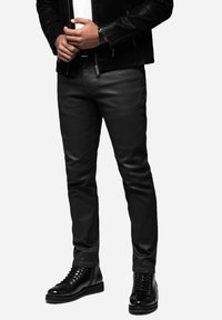 Pantalones de cuero negros combinados con una chaqueta negra con cremallera sobre una camiseta blanca, acompañados de botas negras con cordones, mostrando un diseño elegante.