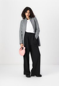 Grijze wollen blazer, witte shirt, zwarte wijde broek, met een kleine roze tas. Zachte texturen, gestructureerde vormen, contrasterende kleuren.