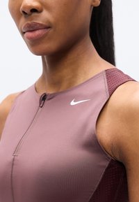 Αθλητική αμάνικη μπλούζα Nike σε απαλό μωβ χρώμα με κλείσιμο με φερμουάρ. Διαθέτει διαπνέον διχτυωτό σχέδιο στους ώμους και λευκή διακριτική λεπτομέρεια με το λογότυπο.