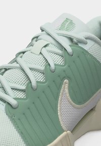 Κοντινό πλάνο αθλητικού παπουτσιού σε ανοιχτό πράσινο και λευκό με πλέγμα στη πάνω πλευρά, σχέδιο με κορδόνια και το λογότυπο Nike στη πλαϊνή επιφάνεια.