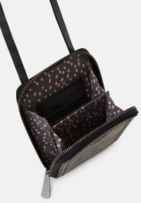 Czarna torebka crossbody z otwartym zamkiem, ukazująca różową wyściółkę w kropeczki i przegródki na karty, z długim czarnym paskiem.