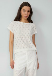 Witte top met korte mouwen, opengewerkte bloemenpatroon, ronde halslijn en losse pasvorm. Gecombineerd met witte geborduurde pantalons. Soepele textuur.