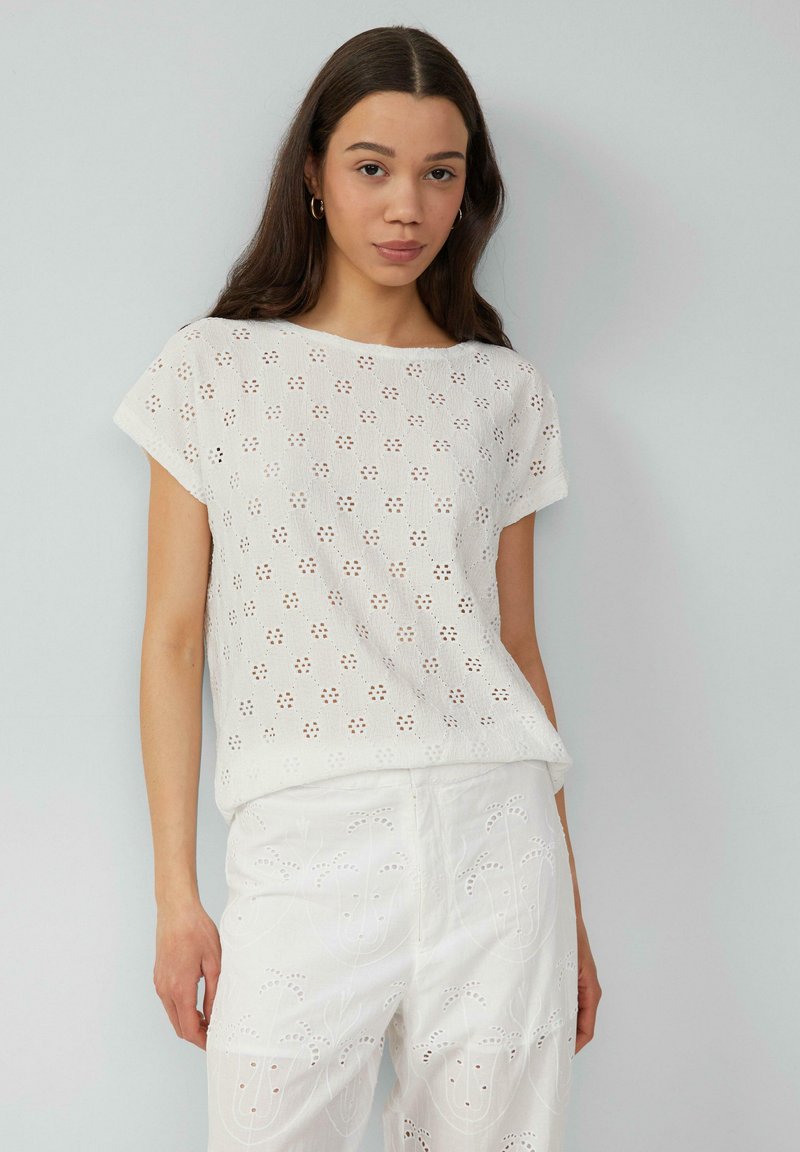 Witte top met korte mouwen, opengewerkte bloemenpatroon, ronde halslijn en losse pasvorm. Gecombineerd met witte geborduurde pantalons. Soepele textuur.