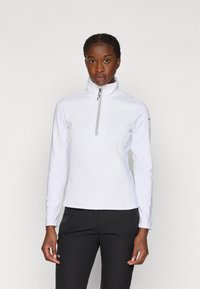 Fleece branco com fecho zip, gola alta, superfície texturizada, mangas compridas e um fecho de contraste. Combinado com calças pretas.